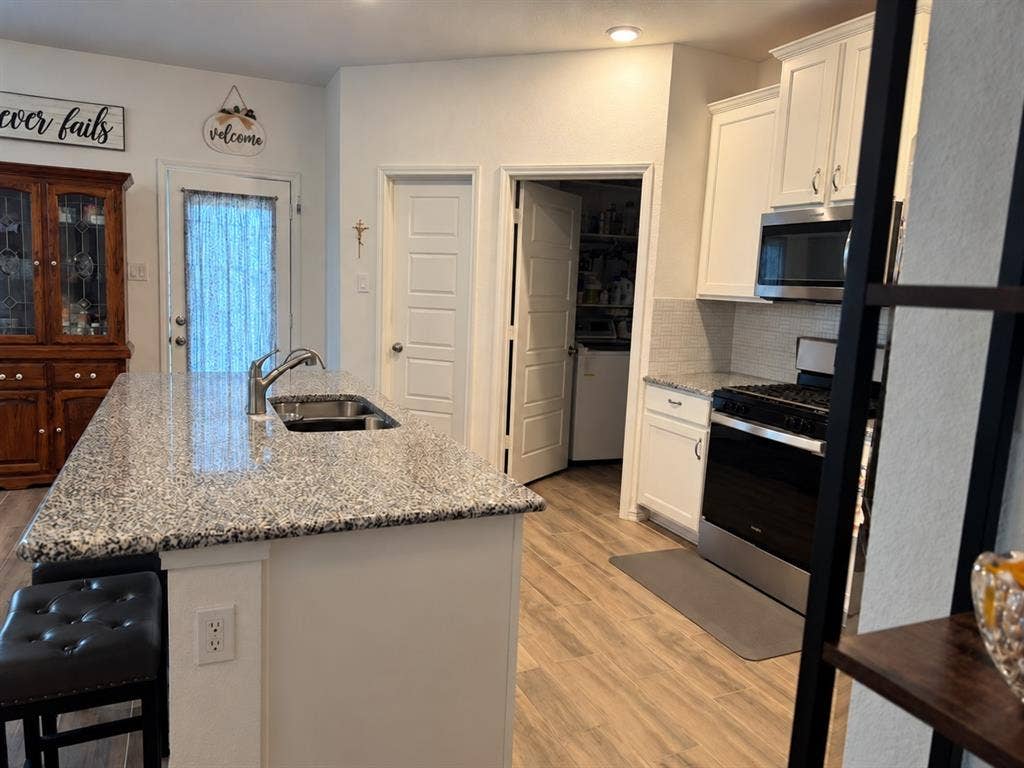 5719 Huffines Boulevard, Royse City, TX 75189 Kitchen featuring a central island with an integrated sink, light-toned countertops, white cabinetry, wood-finish flooring, and a subway tile backsplash