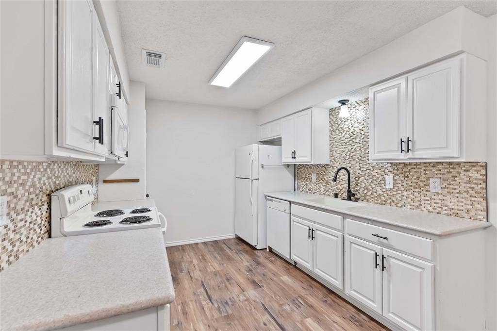 Kitchen featuring white cabinetry, light countertops, mosaic tile backsplash, wood-finish flooring, and white appliances