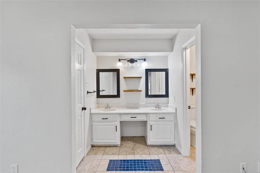 Bathroom featuring a dual vanity with white cabinetry, integrated sinks, black framed mirrors, and a black three-light fixture