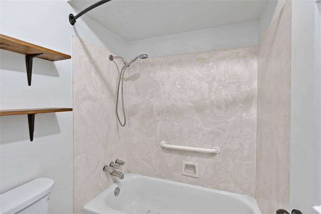 Tub/shower combination featuring a white tub, chrome fixtures, and a light-toned patterned surround