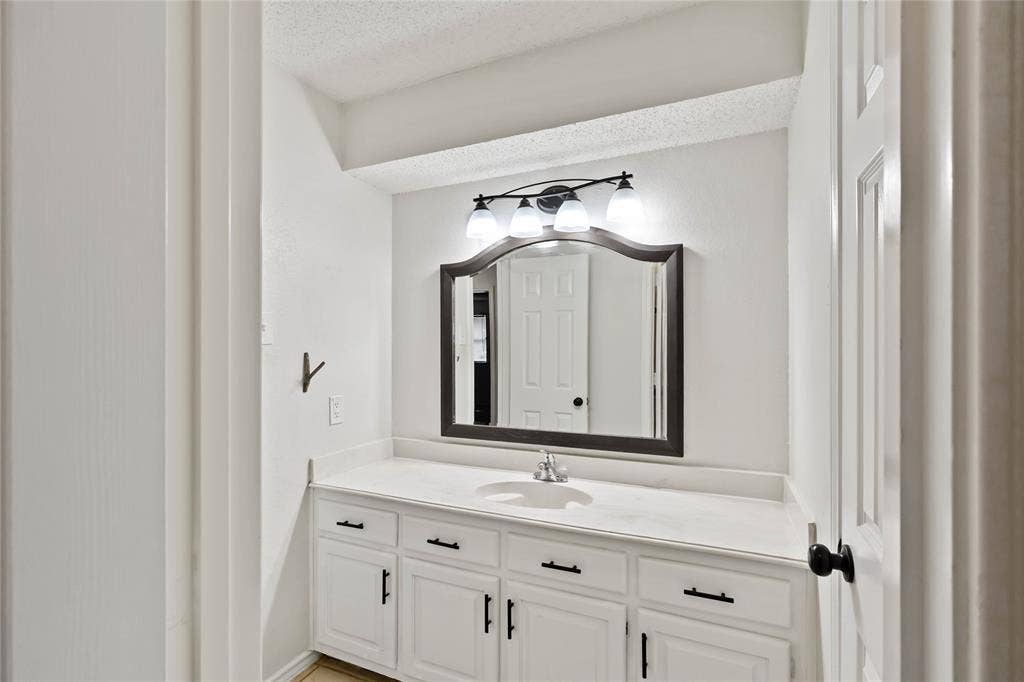 White vanity with integrated sink, modern black hardware, three-light fixture, and arched mirror