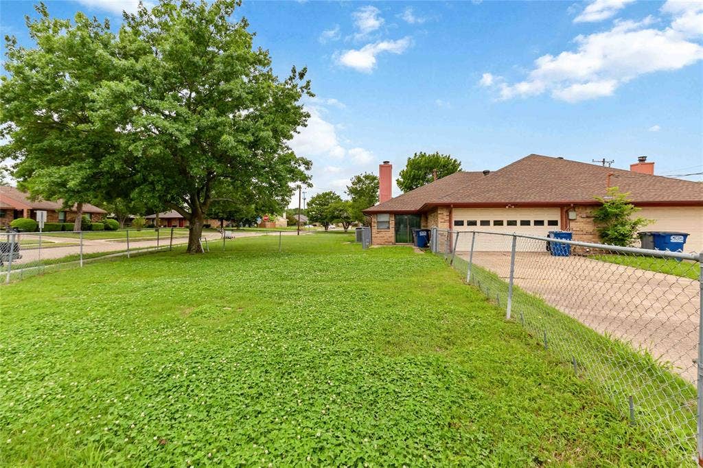 Expansive green lawn featuring a mature tree and chain link fencing