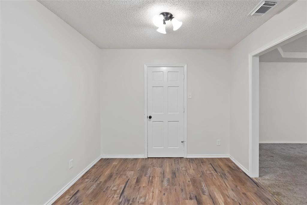 Room featuring wood-finish flooring, white painted walls, a six-panel interior door, and a flush-mount ceiling light fixture