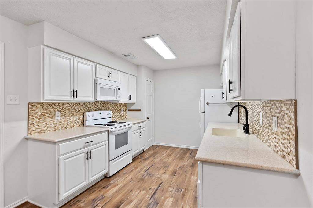 Contemporary kitchen featuring wood-finish flooring, white cabinetry with matte black hardware, and light-colored countertops