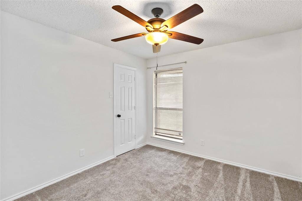 Room featuring a ceiling fan with integrated lighting, textured white walls, and plush gray carpeting