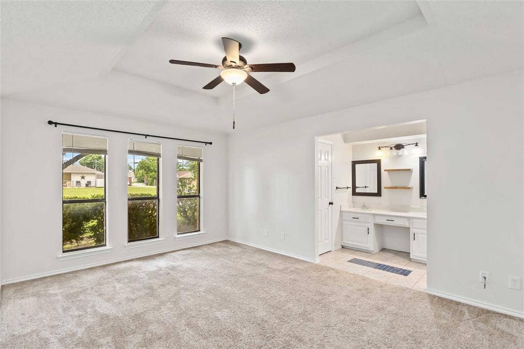 Spacious room featuring a tray ceiling, ceiling fan, and triple windows with outdoor scenery