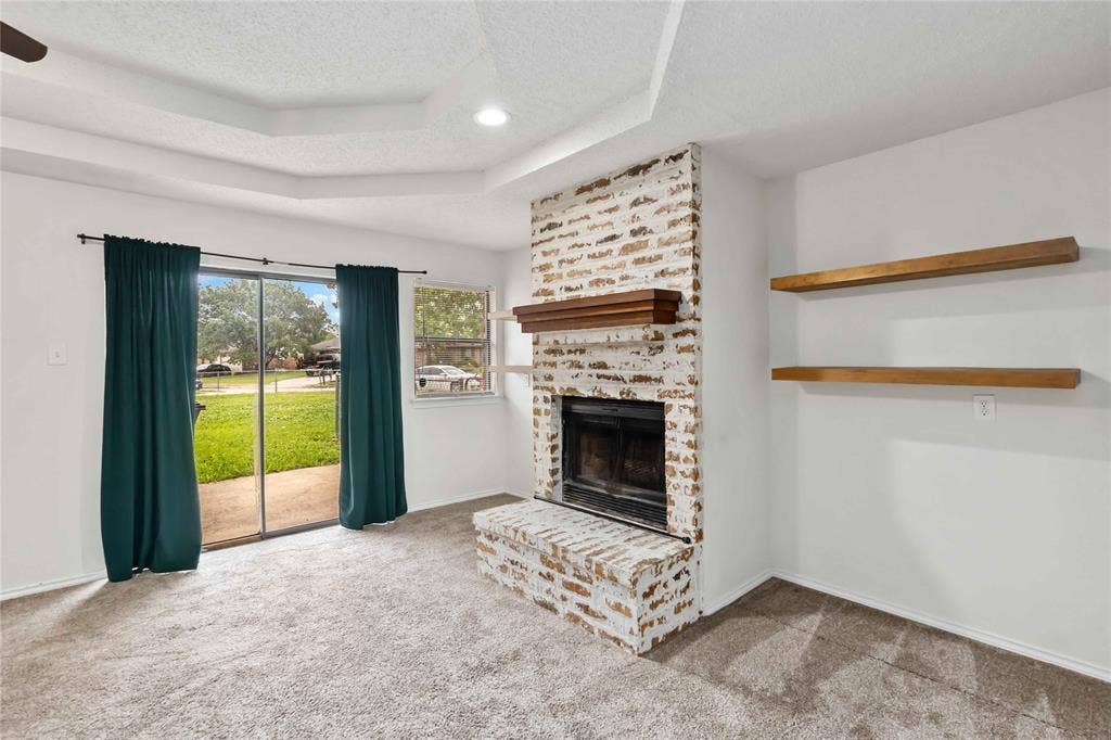 Living space featuring a whitewashed brick fireplace with a wood mantel, tray ceiling, and recessed lighting
