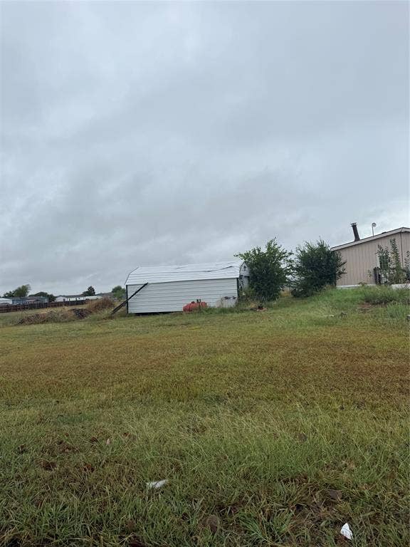 7011 Mitchell Drive, Terrell, TX 75160 Expansive grass area with a metal storage building featuring a curved roof and a separate structure with a visible chimney