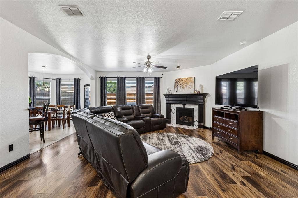 Room to Relax and Unwind – The oversized family room features rich wood-look waterproof laminate flooring, a corner gas fireplace with contrasting black mantel, and an arched opening connecting the breakfast area.