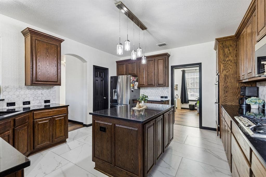 Style and Function in Every Detail – Richly finished cabinetry, sleek dark countertops, and a designer hexagon tile backsplash give this kitchen a distinctive look, while the spacious island provides an ideal surface for meal preparation and serving.