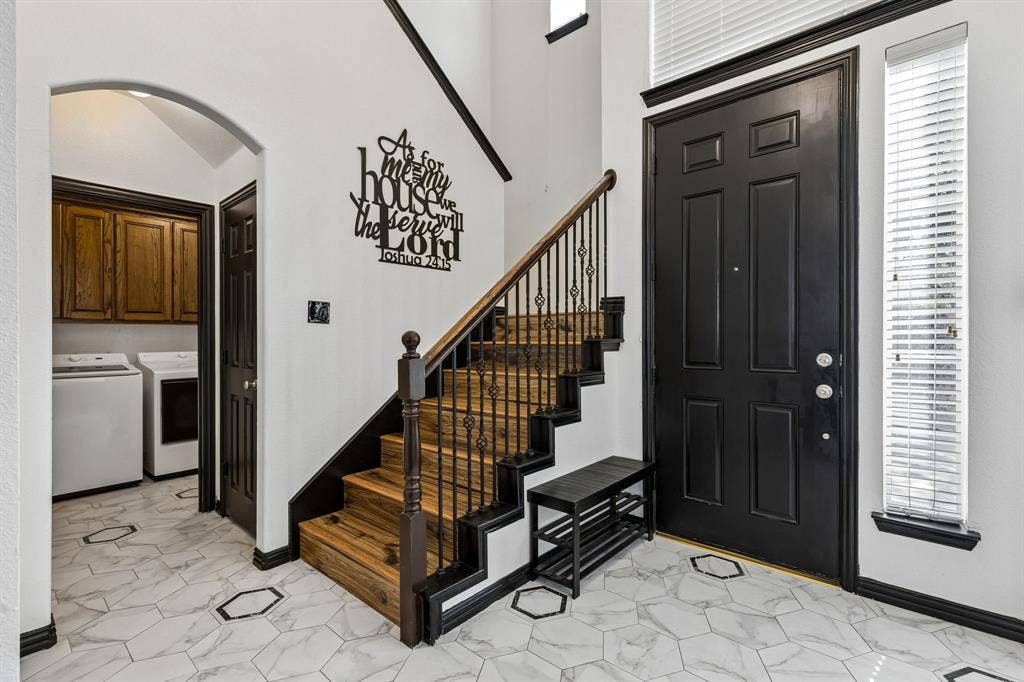 A Welcoming Two-Story Entry – Soaring ceilings create an airy first impression, while the staircase features wood-look treads and decorative iron balusters. The nearby laundry room adds everyday convenience just steps from the front door.
