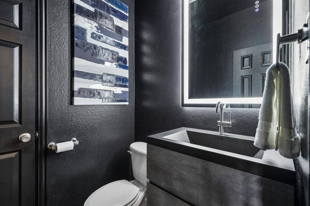 A Powder Bath with Personality – This striking half bath makes a bold statement with black walls, coordinating trim, and a contemporary floating vanity featuring an integrated rectangular sink. An illuminated mirror and modern fixtures complete the updated look.