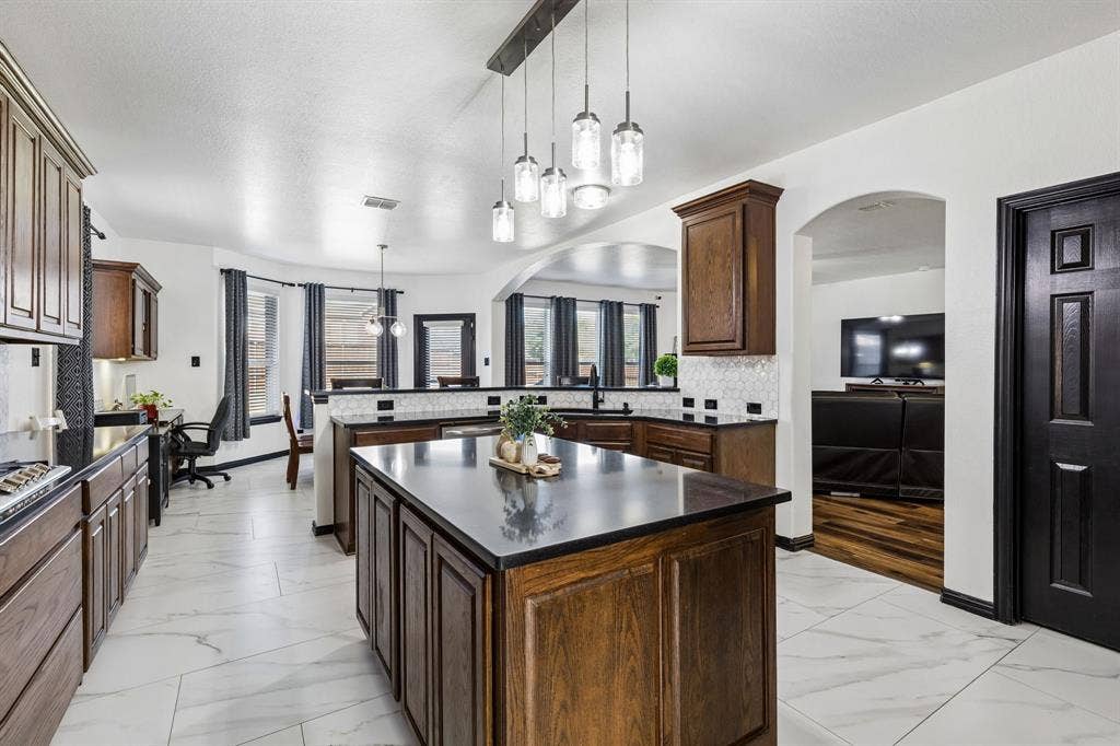 A Kitchen That Brings Everyone Together – The beautifully updated kitchen features a large center island, upgraded custom wood-grain cabinetry, stylish pendant lighting, and generous countertop space, with open sightlines to the adjoining living and dining areas.