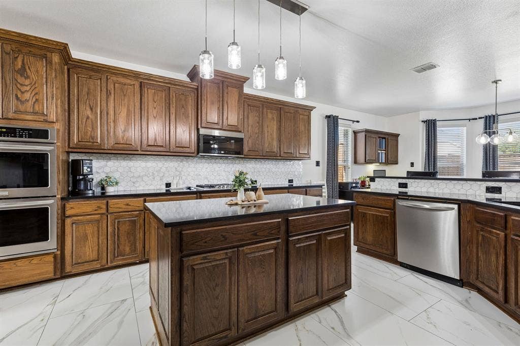 Space to Cook, Serve, and Gather – An expansive island anchors this well-appointed kitchen, complemented by abundant cabinet storage, stainless steel appliances, a designer backsplash, and easy access to the breakfast area with its built-in desk.