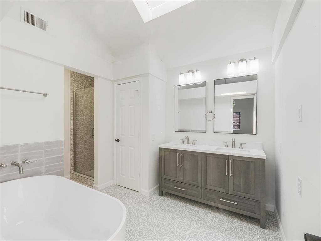 2327 N Ridge Road, McKinney, TX 75072 Spacious bathroom featuring a double vanity with ample storage, a freestanding soaking tub, a glass-enclosed shower, patterned floor tiling, and a skylight