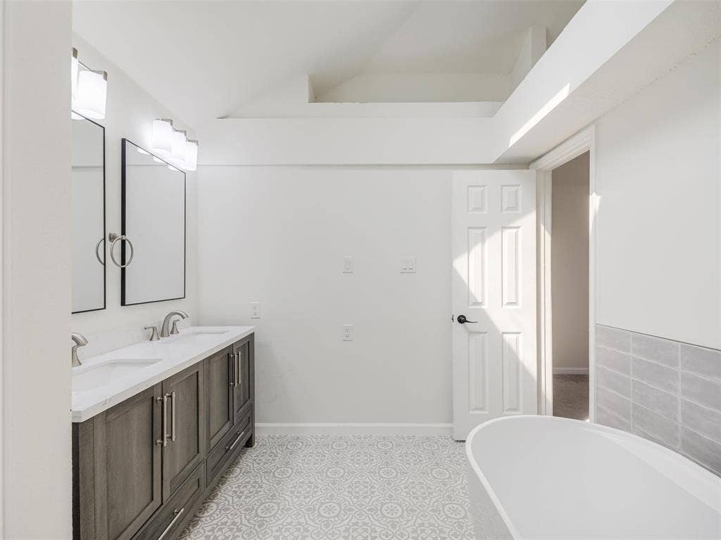2327 N Ridge Road, McKinney, TX 75072 Dual vanity with integrated sinks, patterned tile flooring, freestanding soaking tub, and tile wainscoting