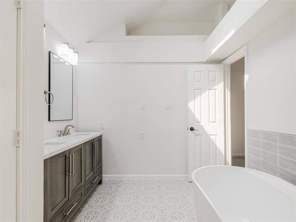 2327 N Ridge Road, McKinney, TX 75072 Dual vanity with undermount sinks, patterned floor tiling, freestanding soaking tub, and an accent wall with light gray rectangular tiles