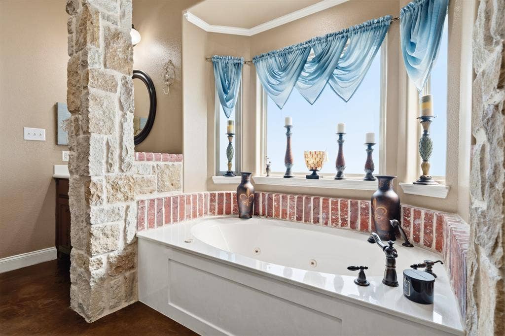 1021 Cascade Trail, McGregor, TX 76657 Built-in soaking tub with a corner window, brick-style surround, and stone accent wall