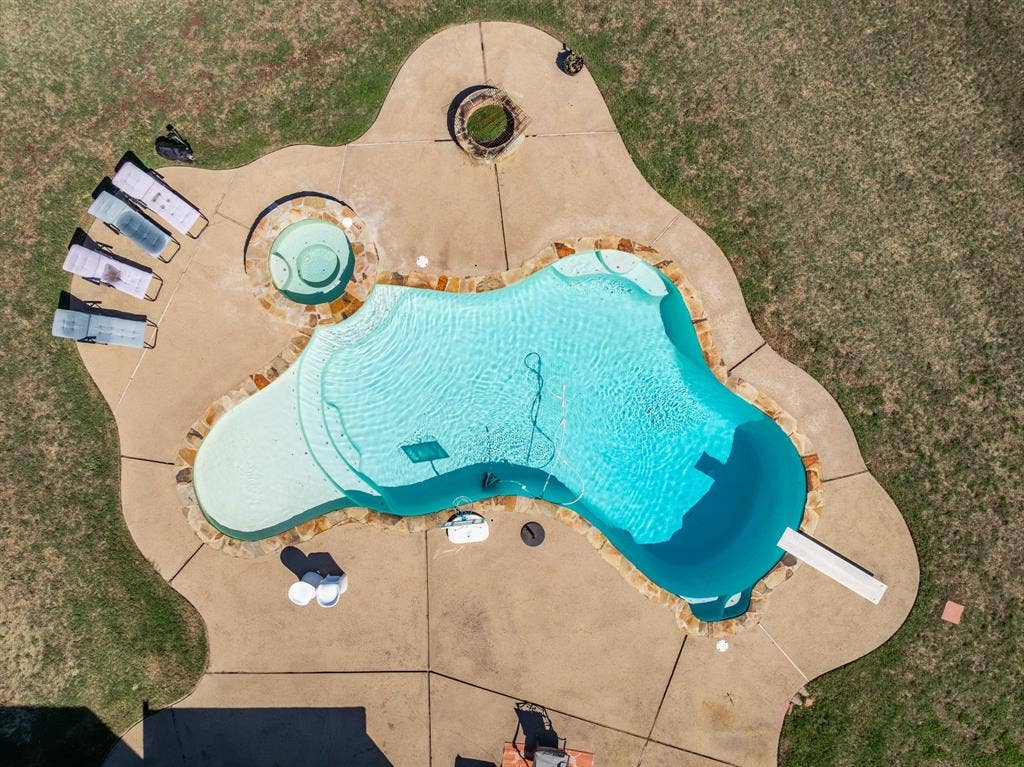 1021 Cascade Trail, McGregor, TX 76657 Freeform swimming pool with integrated spa, diving board, and adjacent fire pit, all surrounded by a concrete deck
