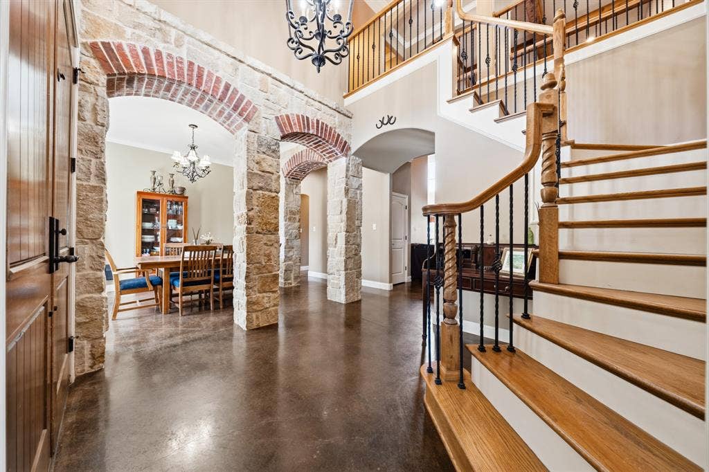 1021 Cascade Trail, McGregor, TX 76657 Stone archways with brick accents, wood-finish flooring, a two-story ceiling, a wrought iron chandelier, and a wood spiral staircase