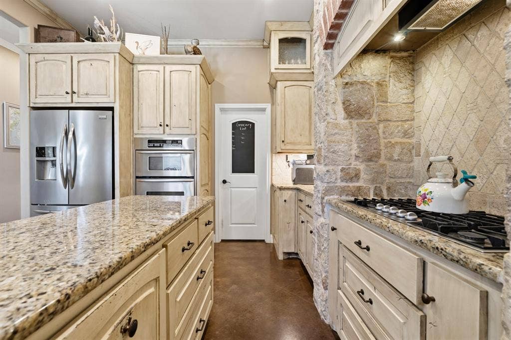 1021 Cascade Trail, McGregor, TX 76657 Granite countertops, stone accent wall, tile backsplash, built-in stainless steel double oven, and a built-in gas cooktop