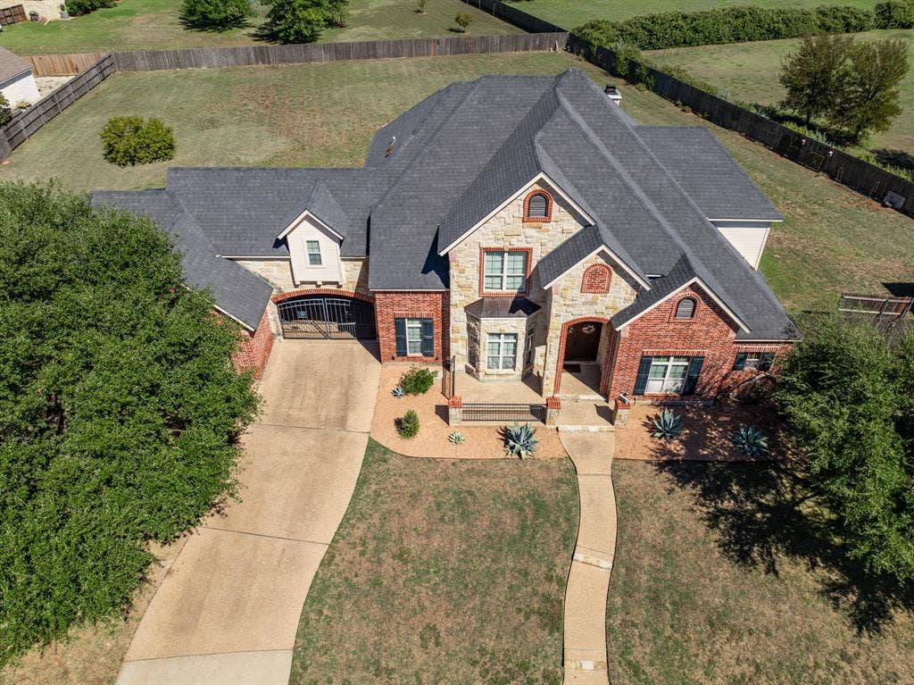 1021 Cascade Trail, McGregor, TX 76657 Stone and brick facade with dark shutters, featuring a prominent front entrance with an arched doorway