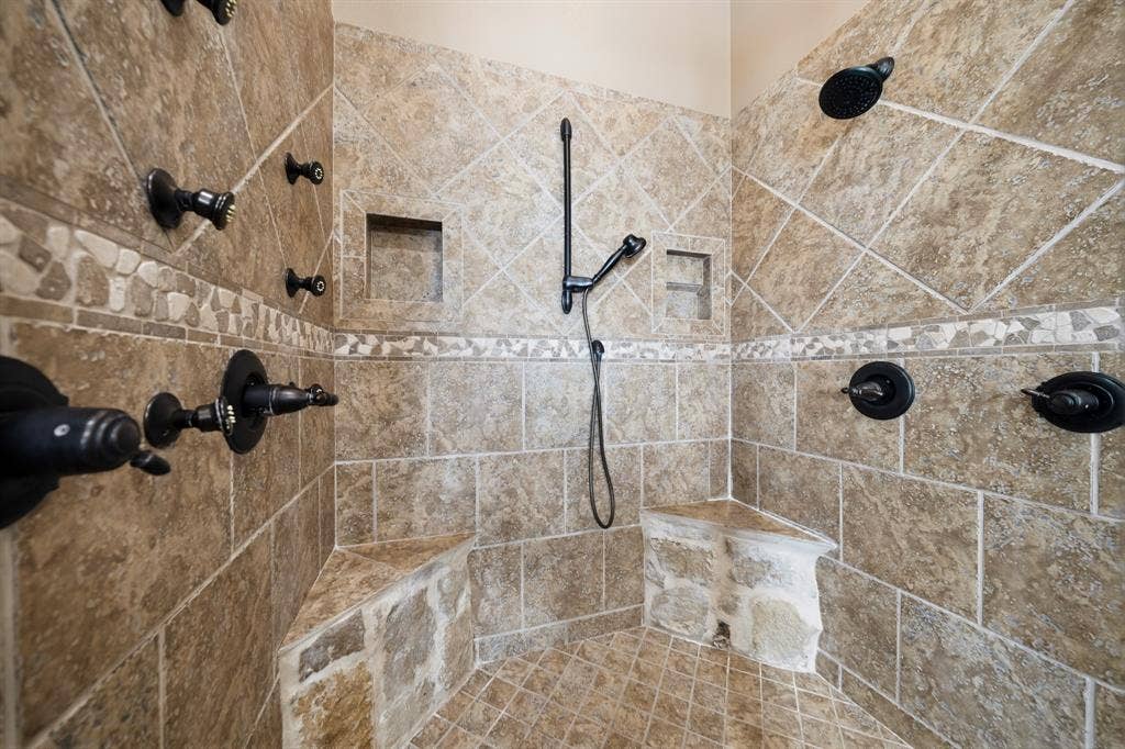 1021 Cascade Trail, McGregor, TX 76657 Tiled shower enclosure featuring multiple shower heads, a handheld shower, integrated tiled seating, and two recessed niches