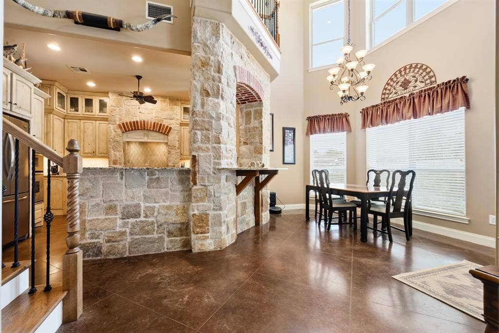 1021 Cascade Trail, McGregor, TX 76657 Two-story ceiling, stone accent walls and archway, wood-finish flooring, staircase with wrought iron balusters, and a kitchen featuring light-toned cabinetry
