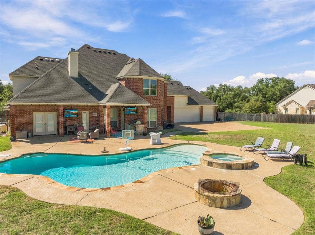 1021 Cascade Trail, McGregor, TX 76657 Brick exterior with a multi-level roofline, featuring a swimming pool, integrated spa, and a stone fire pit