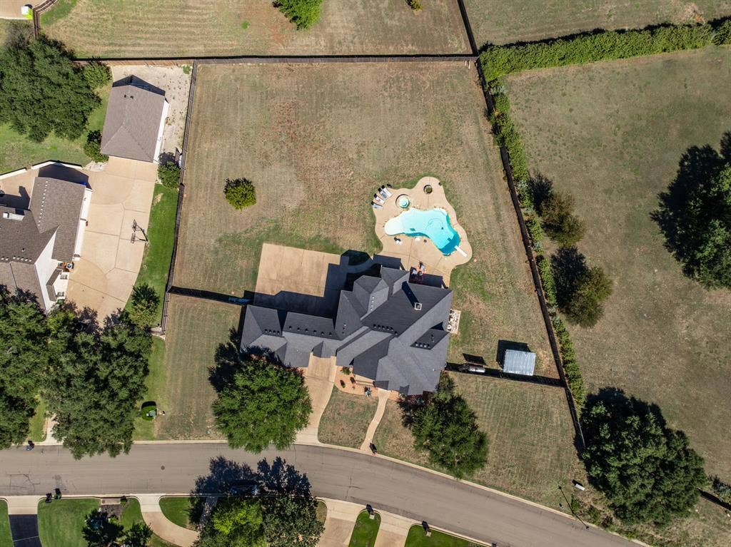 1021 Cascade Trail, McGregor, TX 76657 Expansive property featuring a multi-gabled roofline, a freeform swimming pool with integrated spa, a paved drive, and mature trees