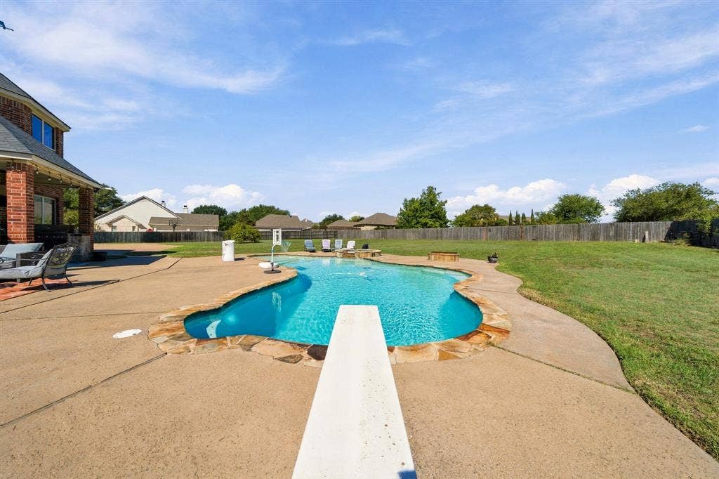 1021 Cascade Trail, McGregor, TX 76657 Curved swimming pool with stone coping, diving board, and expansive concrete patio