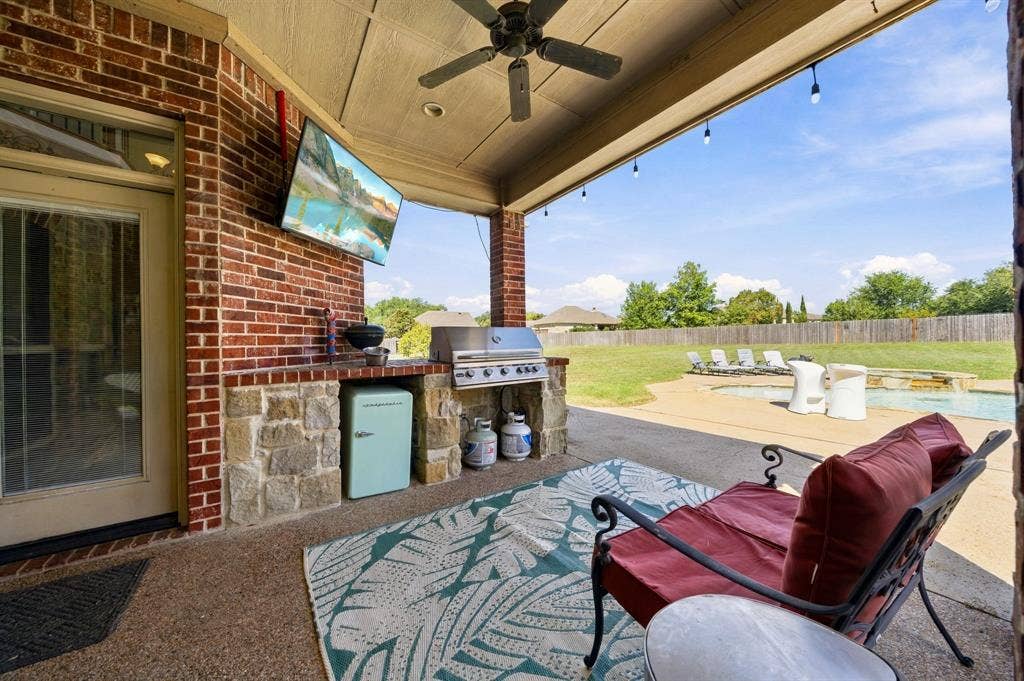 1021 Cascade Trail, McGregor, TX 76657 Covered patio featuring a built-in outdoor kitchen, ceiling fan, and string lights, overlooking a backyard with a swimming pool