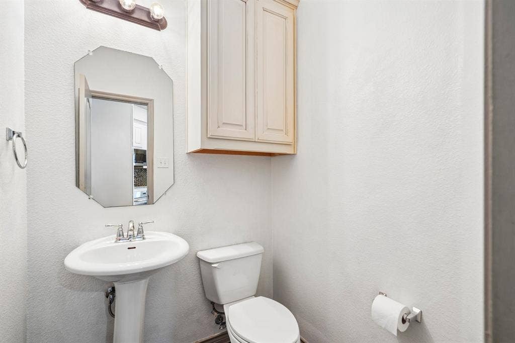 7937 Parkwood Boulevard, Plano, TX 75024 Pedestal sink with chrome faucet, octagonal mirror, built-in cabinetry, and wall-mounted light fixture