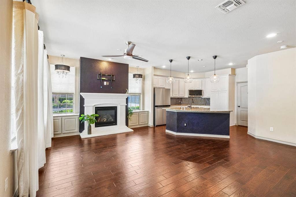 7937 Parkwood Boulevard, Plano, TX 75024 Expansive living area featuring rich wood-finish flooring, a white mantel fireplace, and a ceiling fan