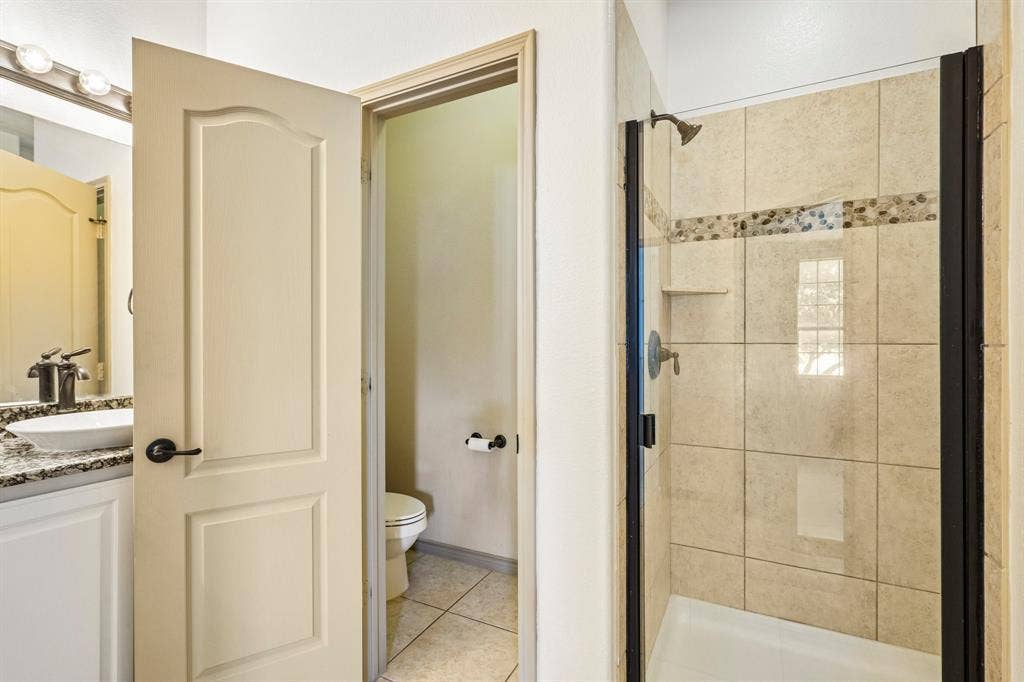 7937 Parkwood Boulevard, Plano, TX 75024 Shower with a glass enclosure, tiled walls featuring a decorative mosaic band, and a built-in shelf