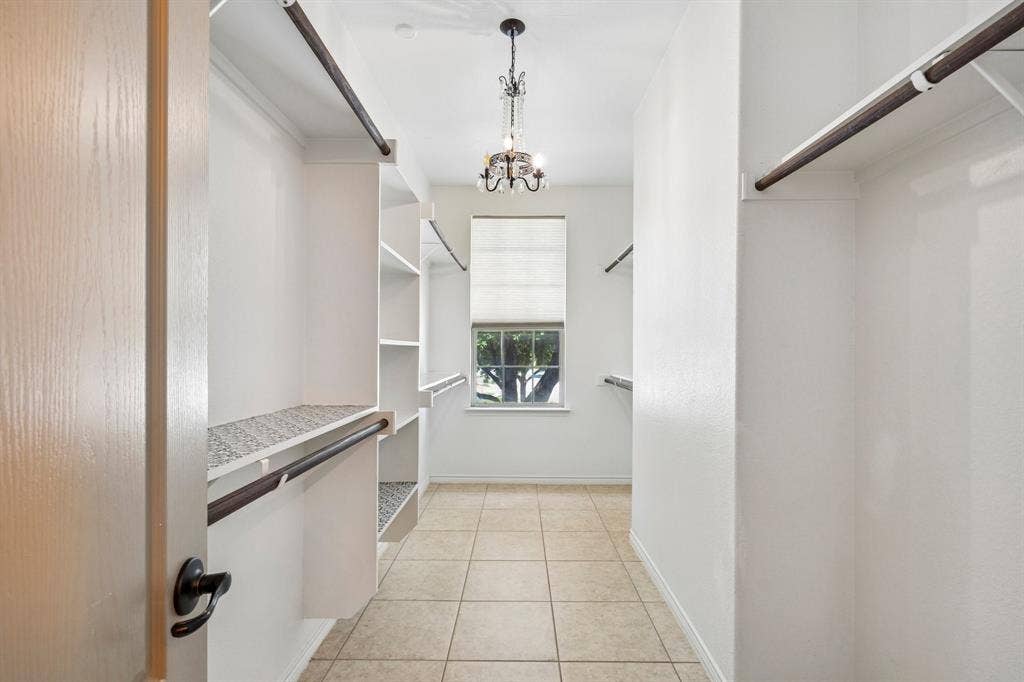 7937 Parkwood Boulevard, Plano, TX 75024 Spacious walk-in closet featuring built-in shelving, hanging rods, tile flooring, a window with a roman shade, and a decorative chandelier