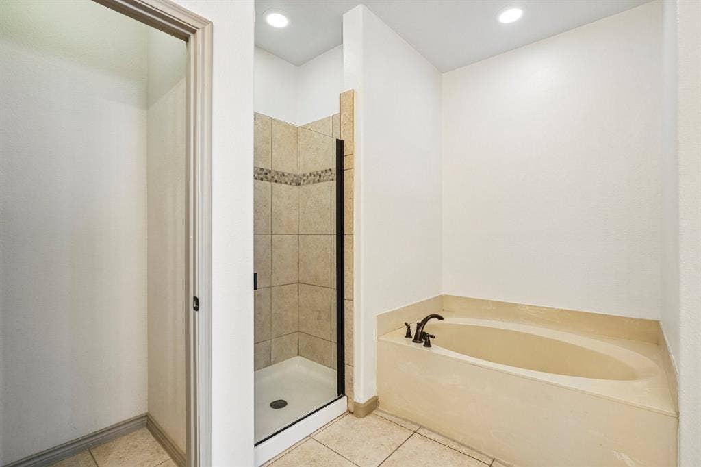 7937 Parkwood Boulevard, Plano, TX 75024 Tiled walk-in shower with a glass enclosure, separate soaking tub with bronze-finish fixtures, recessed lighting, and tile flooring