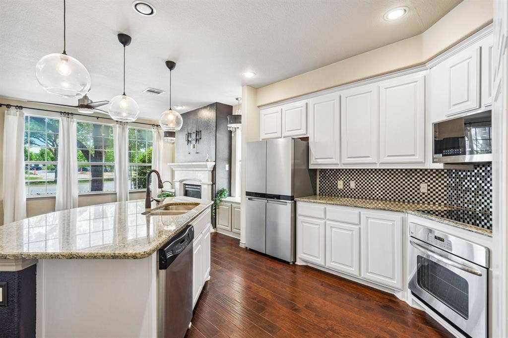 7937 Parkwood Boulevard, Plano, TX 75024 Kitchen featuring a large central island with granite countertops, stainless steel appliances, white cabinetry, and wood-finish flooring