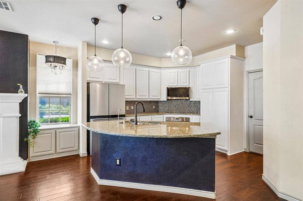 7937 Parkwood Boulevard, Plano, TX 75024 Kitchen island with a light-toned countertop, dark wood-finish flooring, white cabinetry, a dark mosaic tile backsplash, and stainless steel appliances