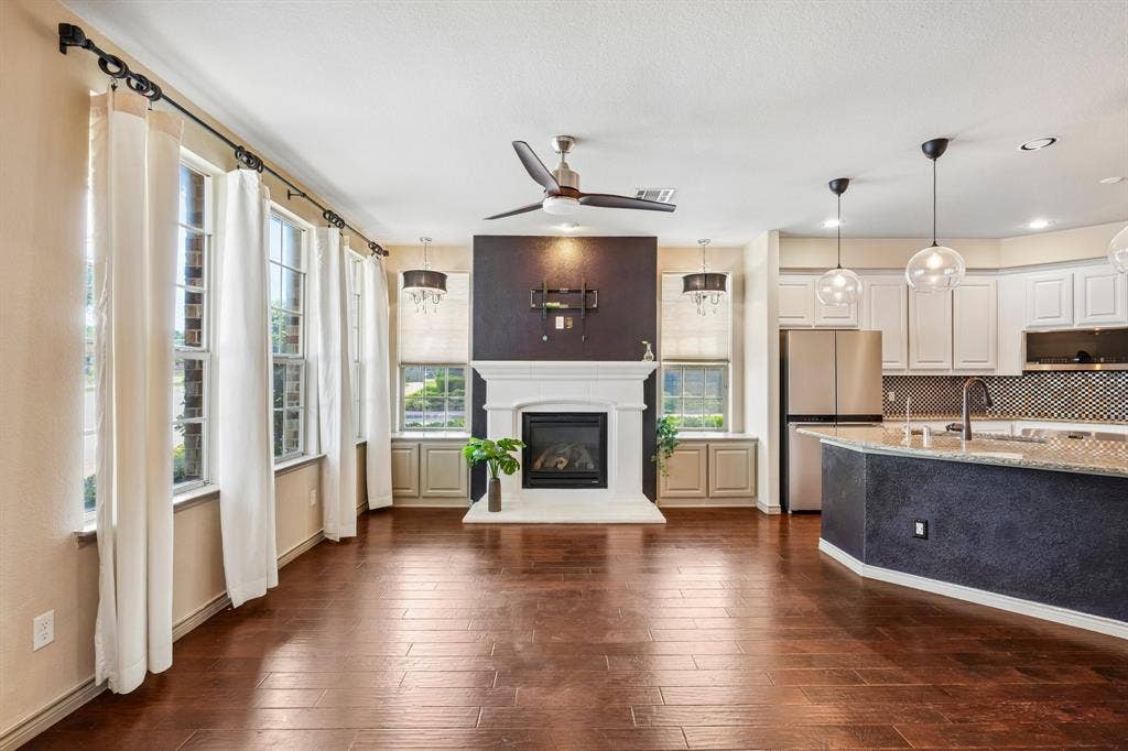 7937 Parkwood Boulevard, Plano, TX 75024 Wood-finish flooring, white mantel fireplace, stainless steel appliances, white cabinetry, and a kitchen island with pendant lighting