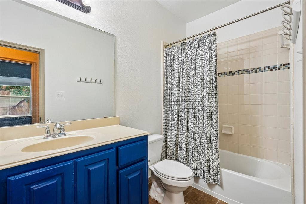 7937 Parkwood Boulevard, Plano, TX 75024 Vanity with integrated sink, vibrant blue cabinetry, large wall mirror, and a tiled shower-tub combination with decorative accent band