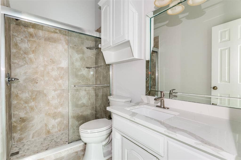 6315 Millwood Court, Arlington, TX 76016 Glass-enclosed shower with stone-look tile, white vanity with integrated sink, quartz-finish countertop, and brushed nickel faucet