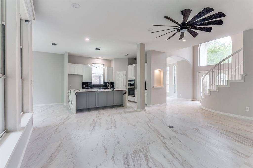 6315 Millwood Court, Arlington, TX 76016 Expansive open-concept space featuring large format tile flooring, a kitchen island with stone waterfall countertop, built-in double ovens, and a grand curved staircase
