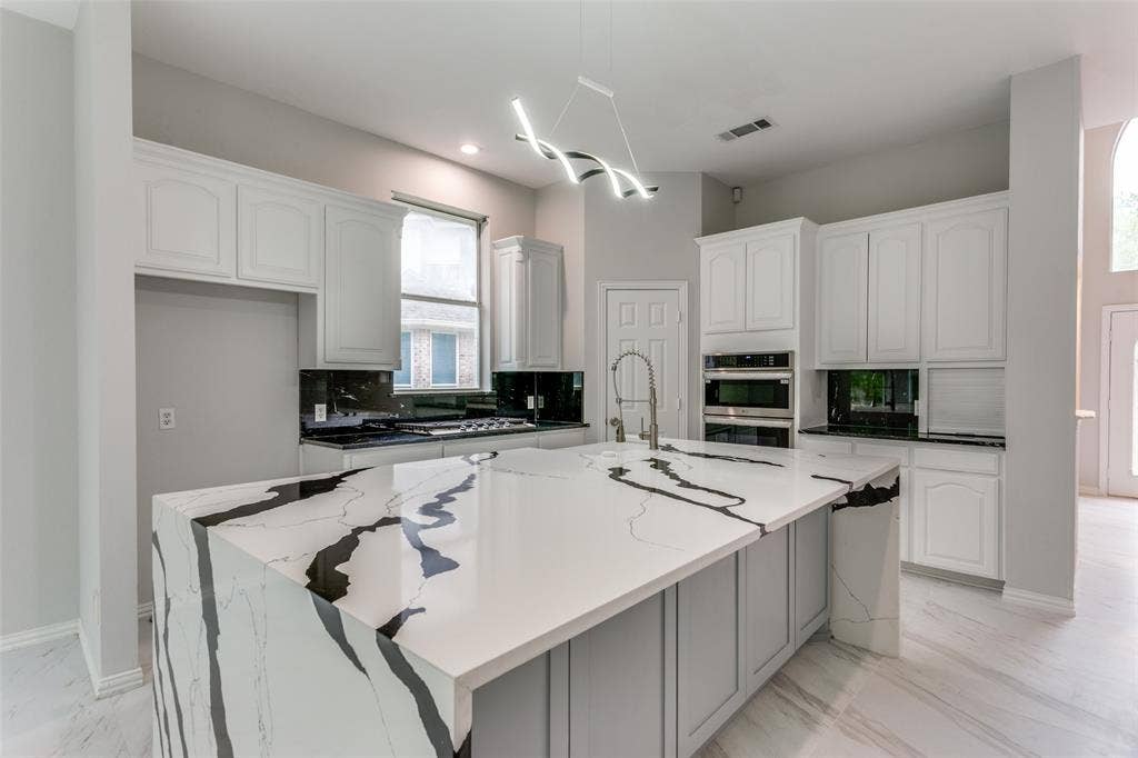 6315 Millwood Court, Arlington, TX 76016 Spacious kitchen featuring a waterfall island with an integrated sink and modern faucet, white cabinetry, a built-in oven, and a contemporary linear chandelier