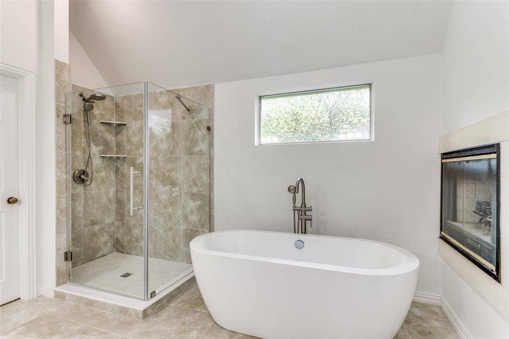 6315 Millwood Court, Arlington, TX 76016 Freestanding soaking tub with floor-mounted faucet, glass-enclosed shower with tile surround, and an inset fireplace