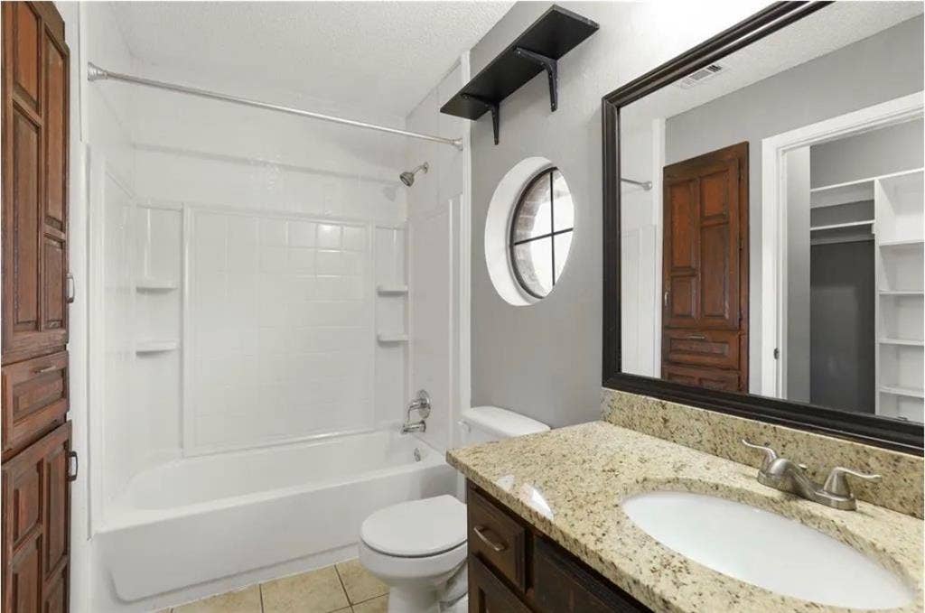 8943 Camfield Way, Frisco, TX 75033 Bathroom featuring a shower-tub combination, a round window, a vanity with a granite countertop, and a built-in storage cabinet