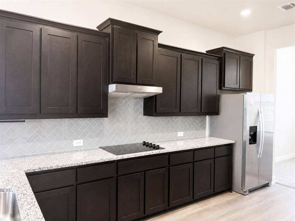6002 14th Street, Midlothian, TX 76065 Modern kitchen with dark wood-finish cabinetry, light speckled countertops, and a herringbone tile backsplash