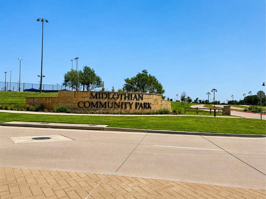 6002 14th Street, Midlothian, TX 76065 Midlothian Community Park entrance featuring a welcoming stone monument sign, expansive manicured lawn, mature landscaping with established trees, professional lighting infrastructure, and well-defined paved pathways throughout the grounds