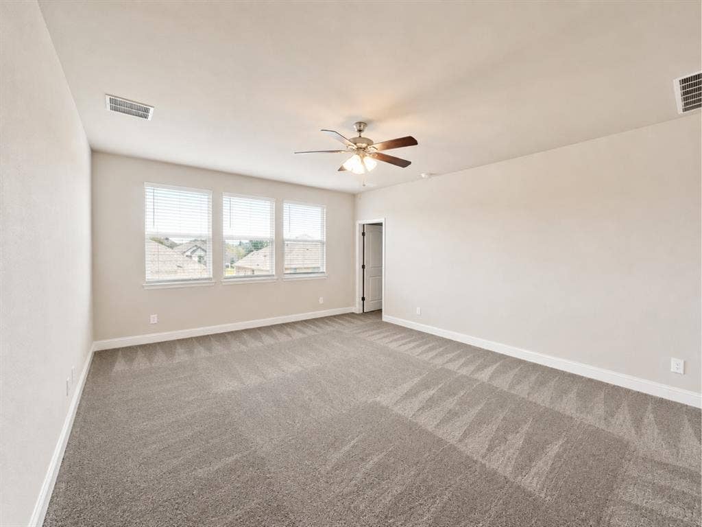 6002 14th Street, Midlothian, TX 76065 Spacious room featuring neutral paint, gray carpeting, triple windows with blinds, a ceiling fan, and white trim