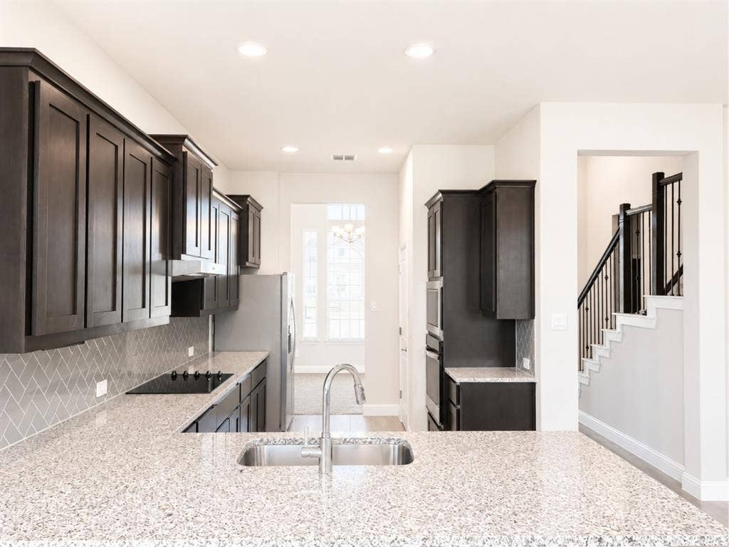 6002 14th Street, Midlothian, TX 76065 Gourmet kitchen featuring dark cabinetry with recessed panel doors, quartz countertops, a dual-basin undermount sink with polished chrome faucet, and a geometric tile backsplash